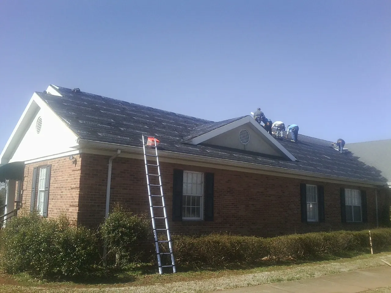 Crew tearing shingles off a brick ranch roof with a ladder set — Emergency Roof Repair work by our crew in Quitman