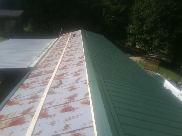 Old rusted panels beside newly installed green metal roofing in Quitman